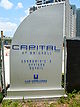 A large, curved, silver sign that reads «Capital at Brickell Condominiums Offices Retail»; a sandy construction site is in the background